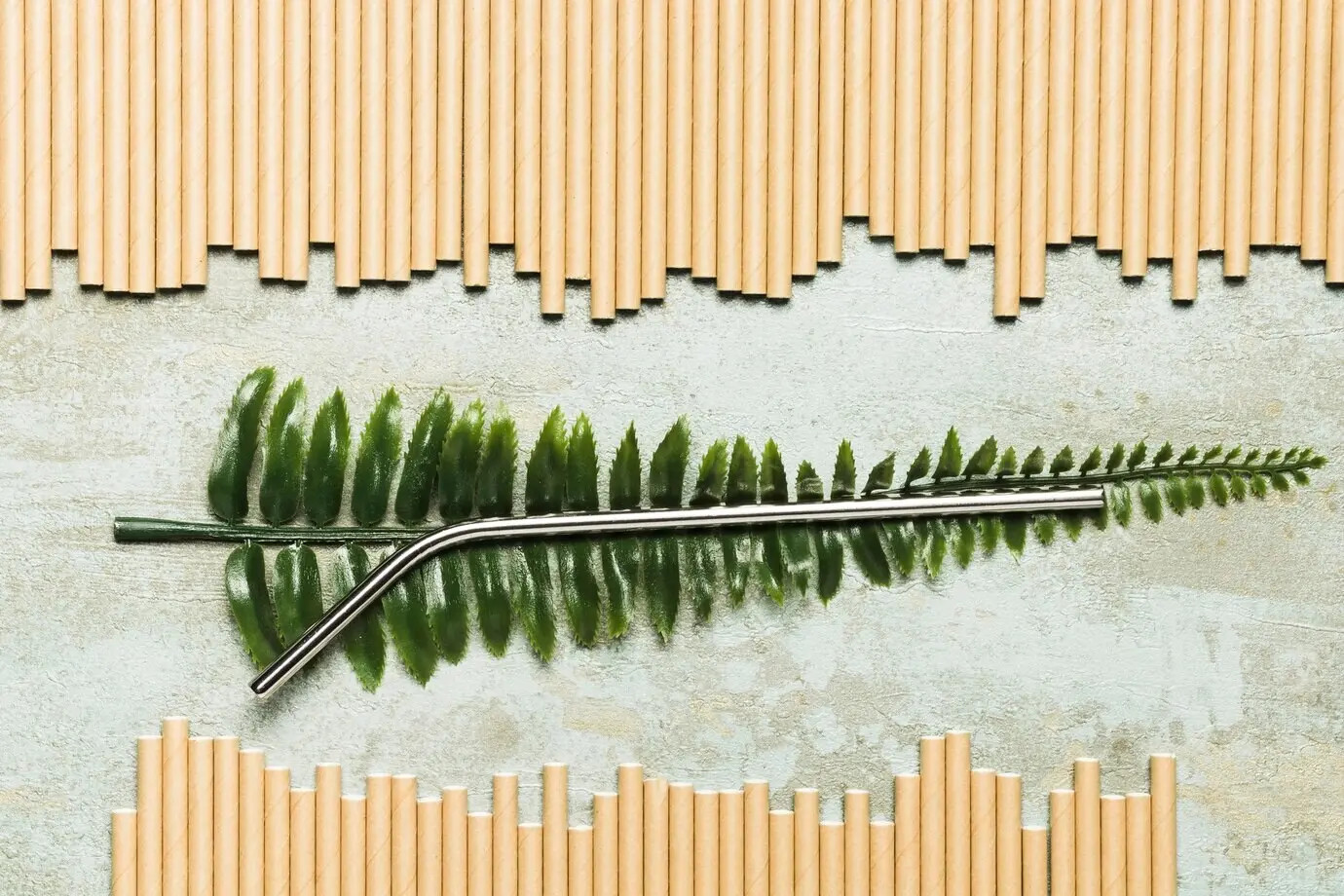 Draufsicht: metallischer Strohhalm auf einem künstlichen Blatt.